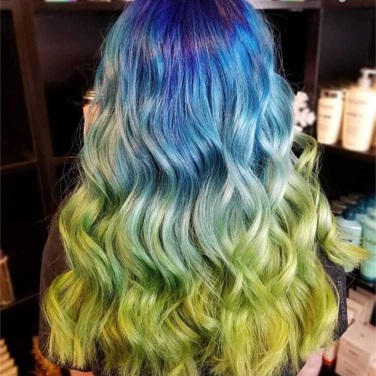 Vibrant blue to green ombre wavy hair against a salon backdrop.
